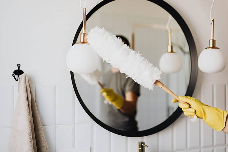 Feather duster being used on a vanity mirror in a bathroom by a cleaner