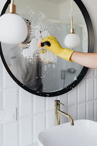 Bathroom mirror being cleaned by someone with soap cleaner and scrubbing pad
