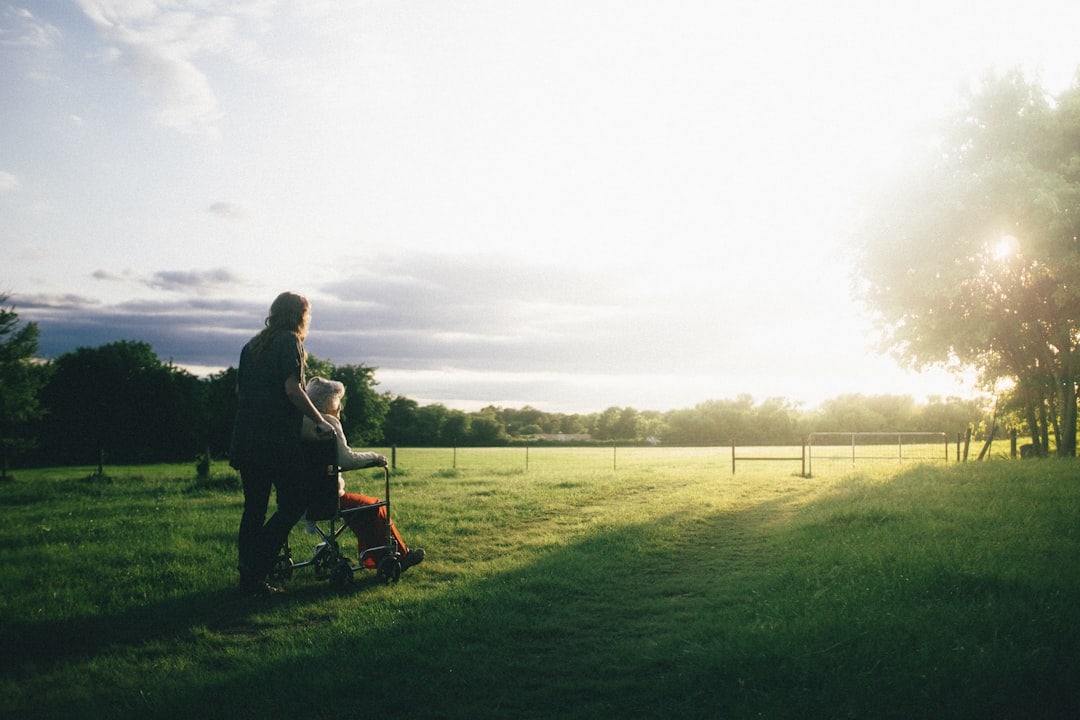 Elderly person receiving gentle support and care assistance while spending time outdoors in a garden.