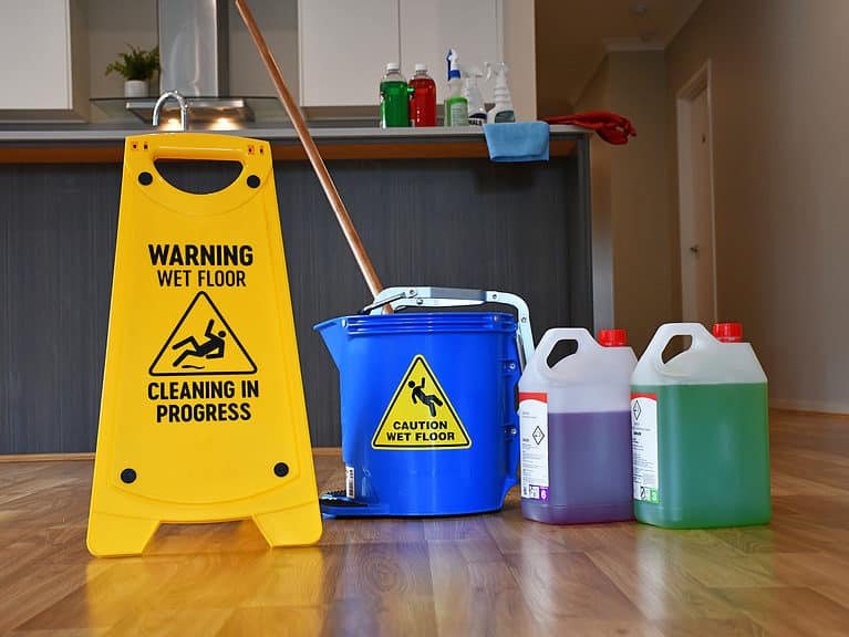 Wet floor warning sign, cleaning supplies, and mops in home cleaning and maintenance setup.