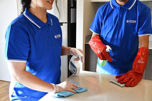 Two people cleaning a kitchen bench top, they are United Home Service cleaners