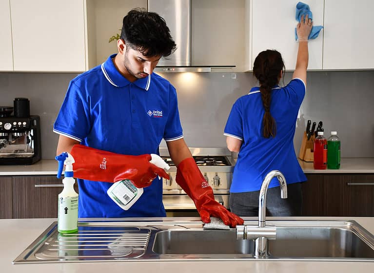 Two United Home Service cleaners attending to a kitchen cleaning the cupboards and sink
