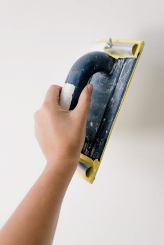 A close-up of a hand using a sanding tool on a white wall for smoothing surfaces.