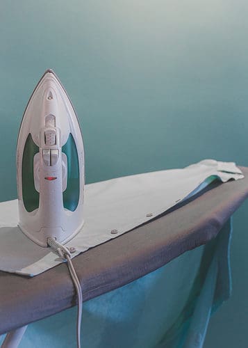 A shirt on an ironing board set up with an iron on top of it